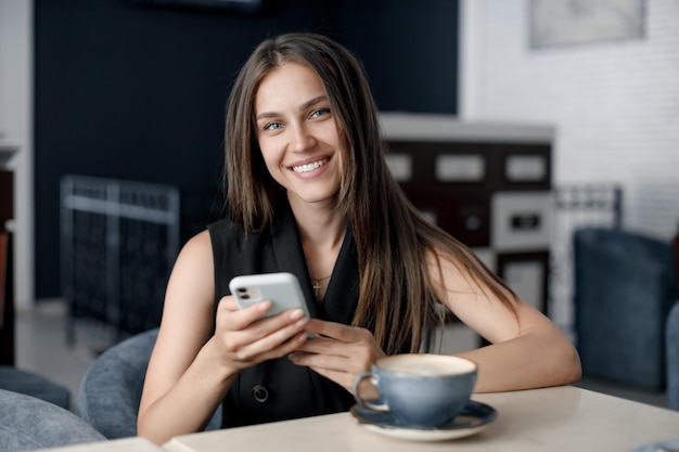 schattige jonge vrouw die lacht in café met mobiele telefoon