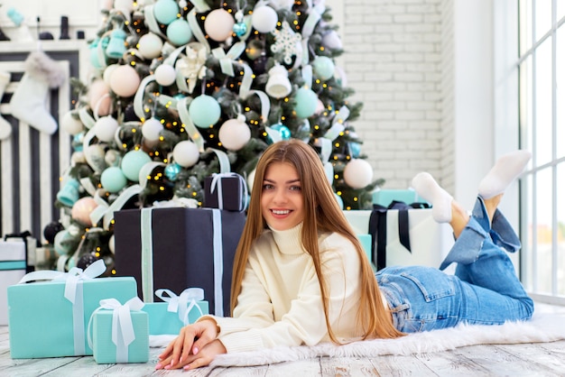 schattige jonge vrouw in de buurt van een kerstboom met kerstcadeaus in een lichte, gezellige kamer