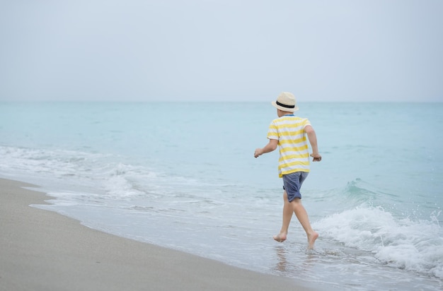 Schattige jongen die op de oceaan of de zee loopt Kind loopt op het strand en speelt met golven