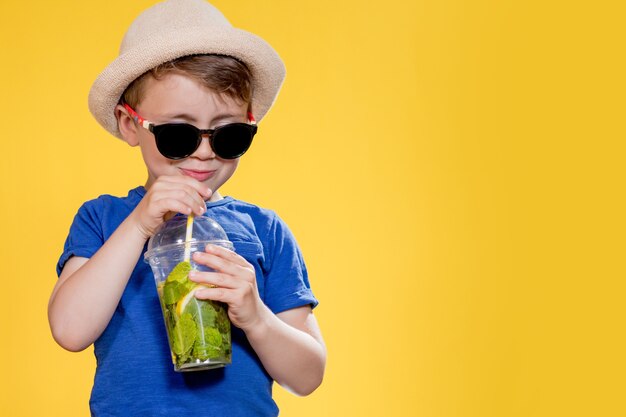 Schattige jongen draagt een zonnebril en drinkt limonade in een plastic beker