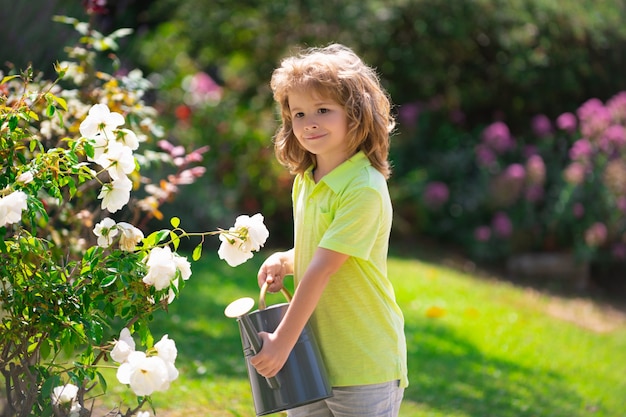 Schattige jongen drenken bloemen in de tuin op zomerdag. Kind met gieter op zomerdag. Kleine helper.