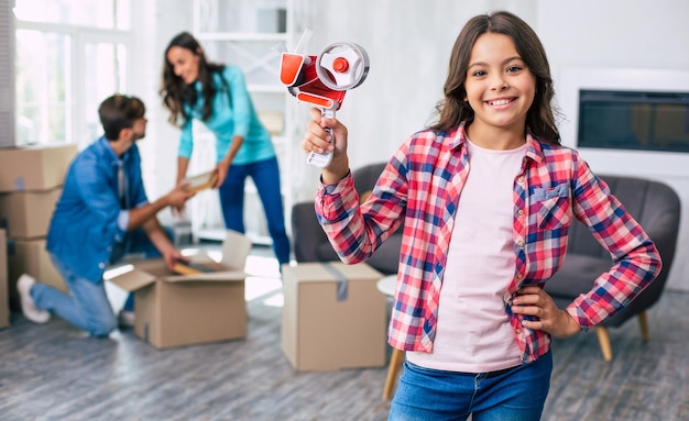 Schattige jongen houdt een plakband in haar hand, klaar om haar ouders te helpen bij het in- of uitpakken van hun persoonlijke spullen in hun nieuwe appartement