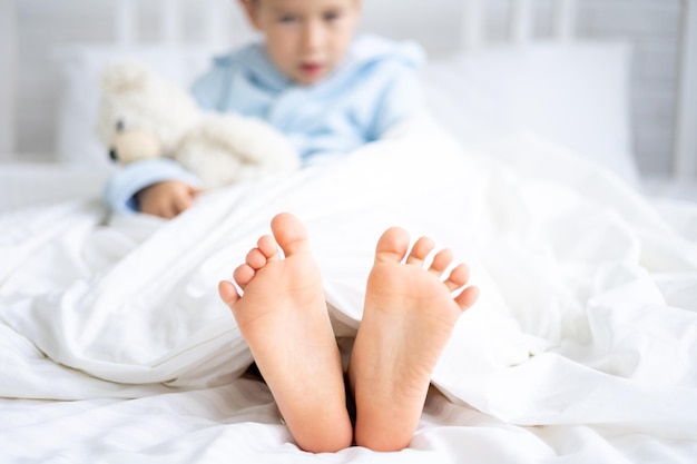 Schattige jongen in een blauwe badjas slaapt 's ochtends thuis in een bed met witte linnen kindernaakte hakken close-up