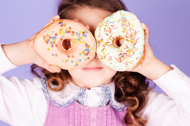 Schattige jongen meisje 4-5 jaar oud met twee lekkere donuts in de kamer. Plezier hebben.