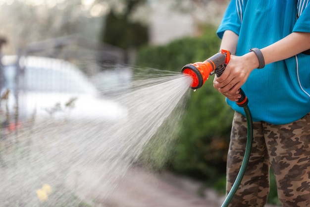 Schattige jongen planten water geven uit de slang, maakt een regen in de tuin. kind dat ouders helpt om bloemen te kweken.