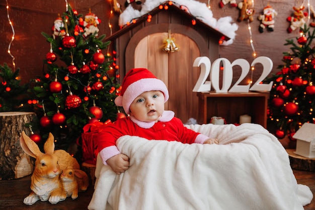 Schattige jongen verkleed als de kerstman zit in de buurt van de kerstboom. goederen voor kinderen en vakanties. Winter Nieuwjaar concept. kerst 2022