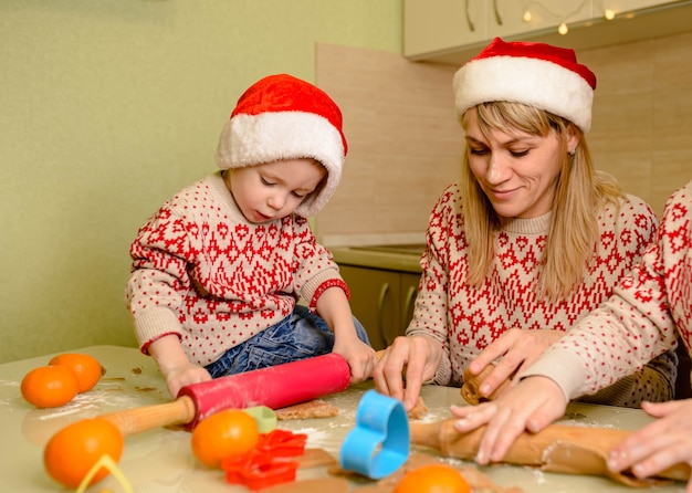 Schattige kinderen en moeder bakken koekjes voor kerstmis. favoriete familietraditie. gelukkig gezin. grappige kinderen bereiden het deeg voor en bakken peperkoekkoekjes in de keuken