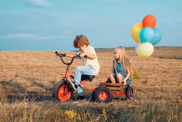 Schattige kinderen op retro fiets tegen blauwe hemelachtergrond op veld kinderen zijn dol op kinderen die plezier hebben op het platteland