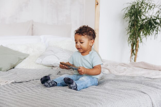 Schattige kleine Afro-Amerikaanse jongen met smartphone thuis op bed gelukkig kind tekenfilms kijken op telefoon