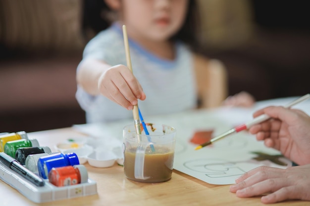 Schattige kleine aziatische baby lacht en haar moeder moeder schilderen met kleurrijke verf met behulp van aquarel aziatisch meisje met penseel tekening kleur baby activiteit levensstijl concept