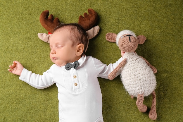 Schattige kleine baby met herten hoorns en speelgoed op kleur