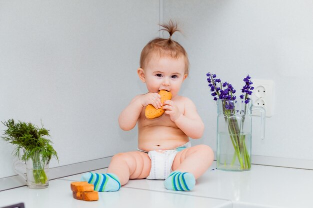 Schattige kleine baby met koekjes zittend op de tafel in de keuken