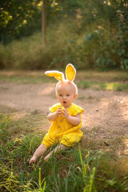 Schattige kleine baby met konijnenoren op Paasdag Het meisje jaagt op paaseieren op het gazon Meisje met paaseieren in de stralen van de ondergaande zon