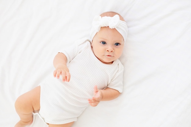 schattige kleine baby op een wit bed thuis in een bodysuit op de rug liggend en glimlachend pasgeboren baby bovenaanzicht