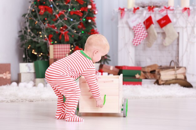 Schattige kleine baby speelt met speelgoedkar in kamer ingericht voor Kerstmis