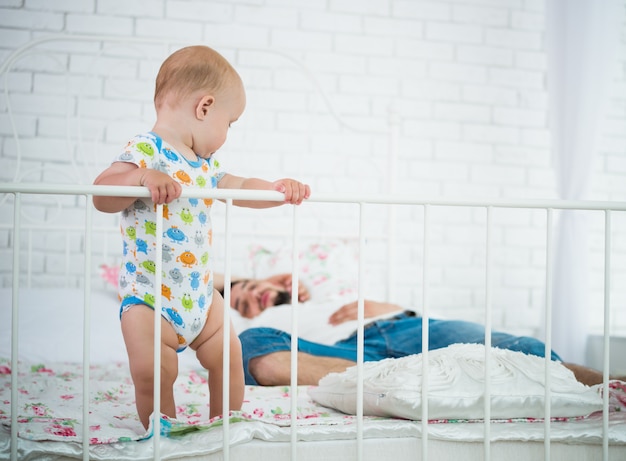 Schattige kleine baby staat op de rand van het bed