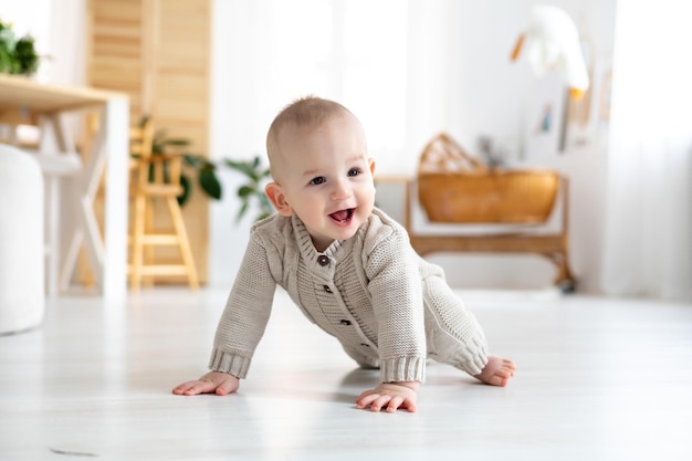 Foto schattige kleine babyjongen in een pastelkleurig wollen gebreid pak dat leert kruipen op de vloer in een lichte woonkamer baby die lacht en vroege ontwikkeling van kinderen speelt