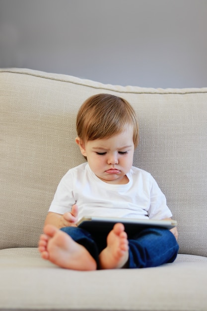 Foto schattige kleine babyjongen met grappige gezichtsuitdrukking kijken cartoons op digitale tablet