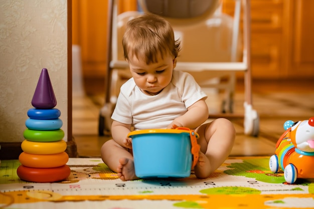 Schattige kleine babyjongen spelen met kleurrijk educatief speelgoed op de speelmat in het interieur