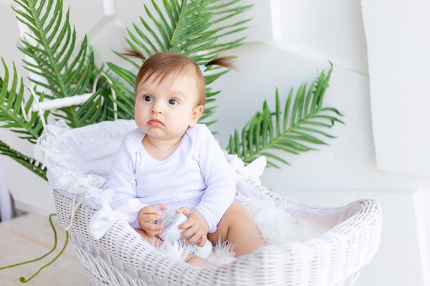 Schattige kleine babymeisje, zittend in een mooie wandelwagen in een witte romper thuis en met een fles melk