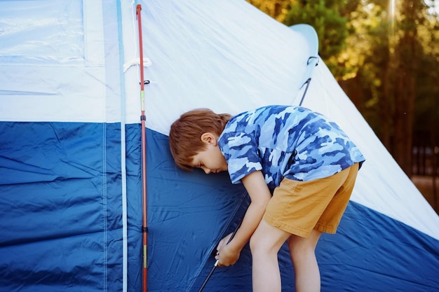 schattige kleine blanke jongen die helpt bij het opzetten van een tent Familiekampeerconcept