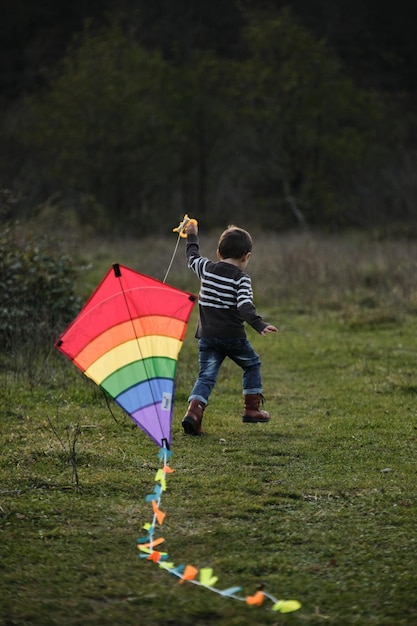 Schattige kleine blanke jongen rent op groen gras in het veld en lanceert veelkleurige gestreepte vlieger