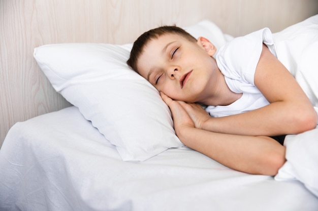 Schattige kleine blanke jongen wordt 's ochtends wakker in zijn comfortabele bed onder zonlicht