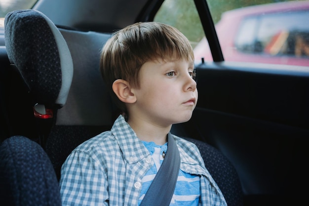 Schattige kleine blanke jongen zittend in kinderzitje reizen met de auto moe en verveeld