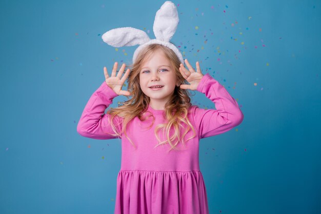 Schattige kleine blonde meisje in Easter bunny oren in roze jurk op een blauwe achtergrond.