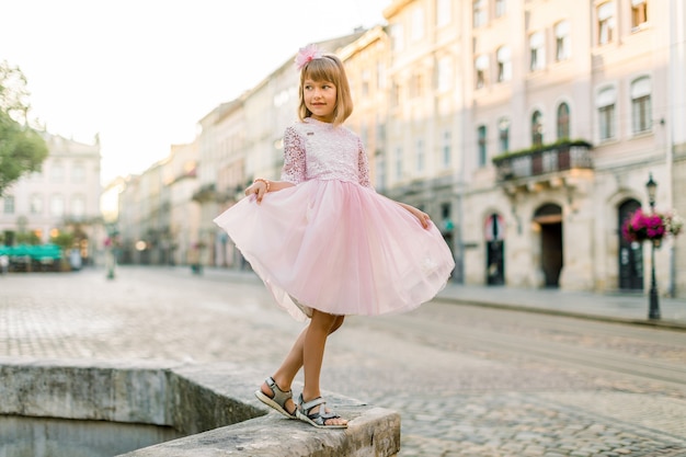 Schattige kleine blonde meisje in een roze jurk in de stad