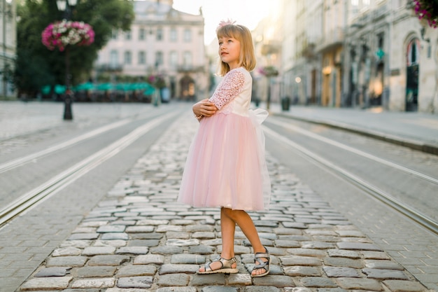 Schattige kleine blonde meisje in een roze jurk in de stad