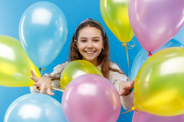 Schattige kleine emotionele meisje in witte kleding met gekleurde ballons op blauw