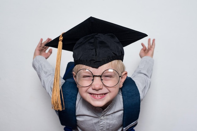 Schattige kleine glimlachende blonde jongen met een bril met een studentenhoed Kinderen onderwijsconcept Basisschool