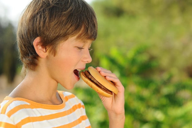 Schattige kleine grappige jongen die hamburger eet met buiten close-up