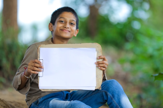 Schattige kleine indiase / aziatische jongen met blocnote met pen