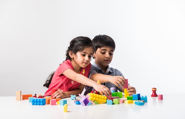 Schattige kleine indiase aziatische kinderen spelen met kleurrijk plastic speelgoed of blokken zittend aan tafel of geïsoleerd op een witte achtergrond white