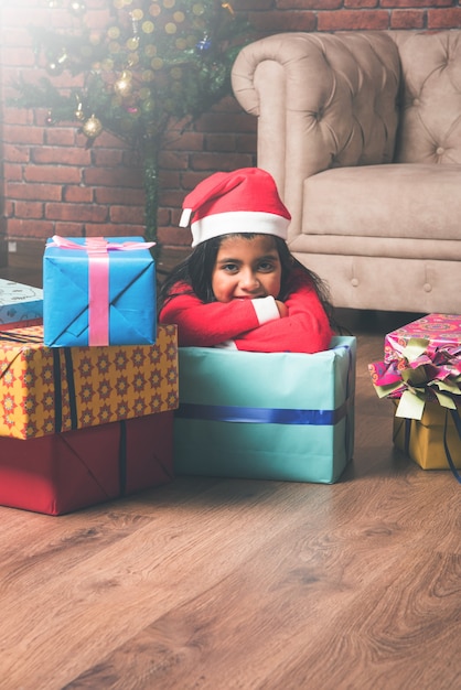 Schattige kleine indiase aziatische kinderen vieren kerstmis thuis met kerstmuts, geschenken en kerstboom