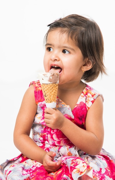 Schattige kleine Indiase Aziatische meisje kind likken of eten van chocolade-ijs in kegel, geïsoleerd op witte achtergrond