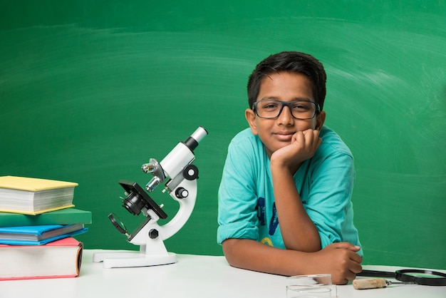 Schattige kleine Indiase Aziatische schooljongen student experimenteert of studeert wetenschap in laboratorium, over groene schoolbordachtergrond met educatieve doodles