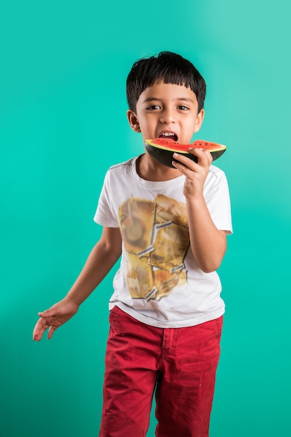 Schattige kleine Indiase jongen die watermeloenplak eet, staande geïsoleerd over groene achtergrond