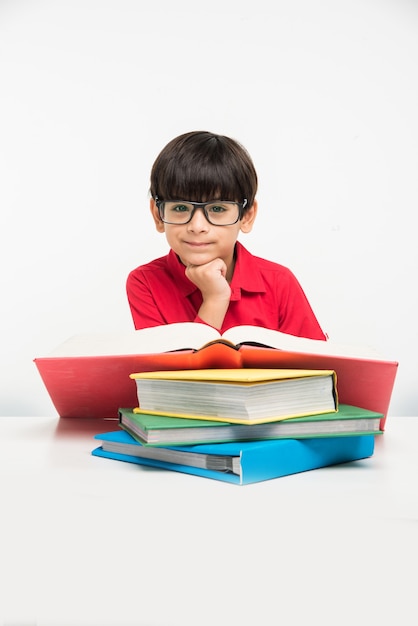 Schattige kleine Indiase of Aziatische jongen die een boek vasthoudt of leest boven de studeertafel of op een witte vloer, geïsoleerd op een witte achtergrond