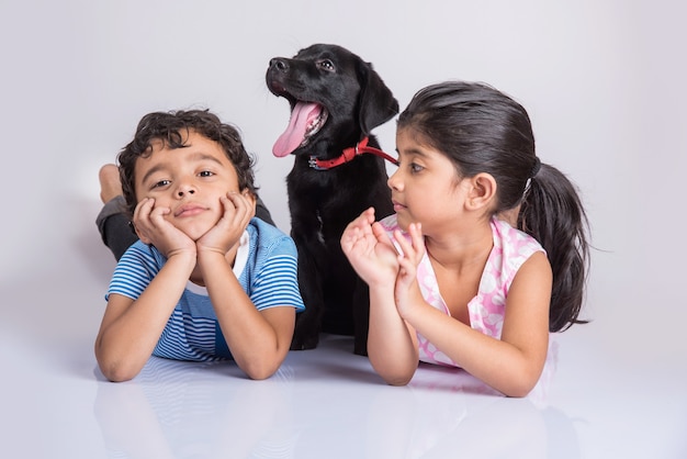 Schattige kleine Indiase of Aziatische jongen en meisje spelen met Black Labrador Retriever pup liggend of zittend geïsoleerd op een witte achtergrond