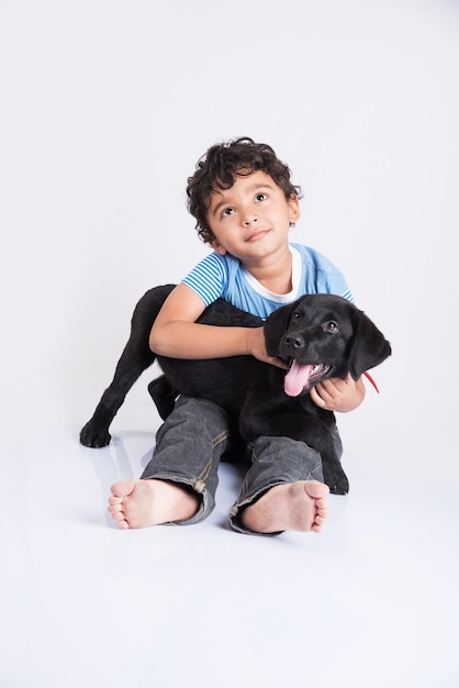 Schattige kleine Indiase of Aziatische jongen spelen met Black Labrador Retriever pup liggend of zittend geïsoleerd op een witte achtergrond