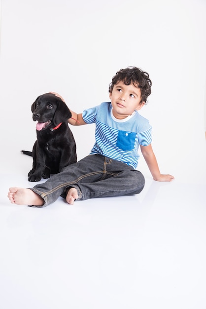 Schattige kleine Indiase of Aziatische jongen spelen met Black Labrador Retriever pup liggend of zittend geïsoleerd op een witte achtergrond