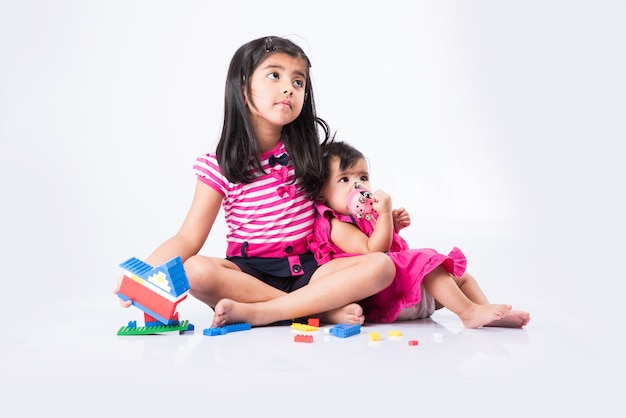 Schattige kleine Indiase of Aziatische kinderen spelen met speelgoed of blokken en hebben plezier terwijl ze aan tafel zitten of geïsoleerd op een witte achtergrond