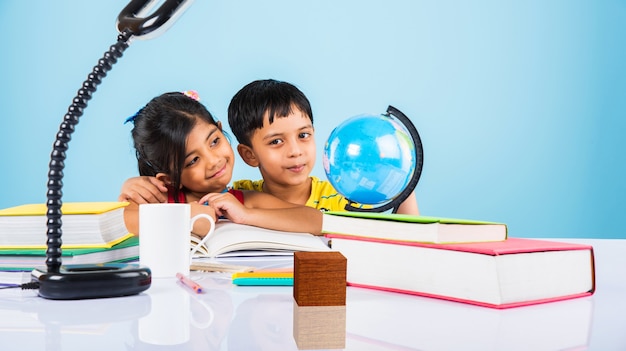 Schattige kleine indiase of aziatische kinderen studeren op studietafel met stapel boeken, educatieve wereld, geïsoleerd over lichtblauwe kleur