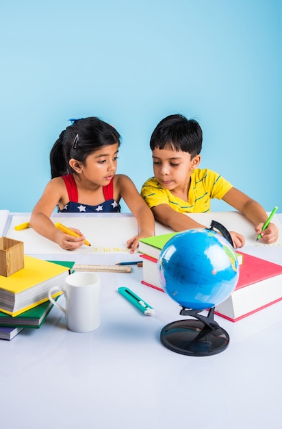 Schattige kleine Indiase of Aziatische kinderen studeren op studietafel met stapel boeken, educatieve wereld, geïsoleerd over lichtblauwe kleur