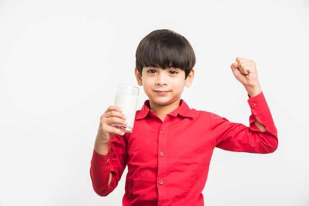 Schattige kleine indiase of aziatische speelse jongen die een glas melk vasthoudt of drinkt, geïsoleerd op witte achtergrond