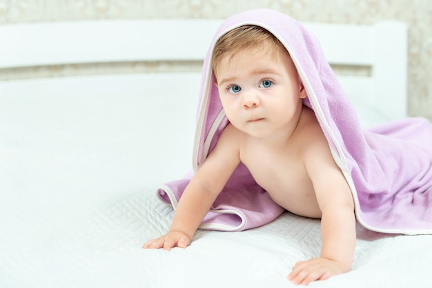 Schattige kleine jongen bedekt met violet handdoek liggend op bed Jeugdbad concept Ernstige emotie