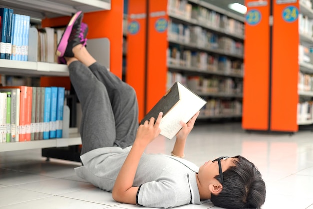 Schattige kleine jongen die op de vloer ligt en een boek leest in de bibliotheek